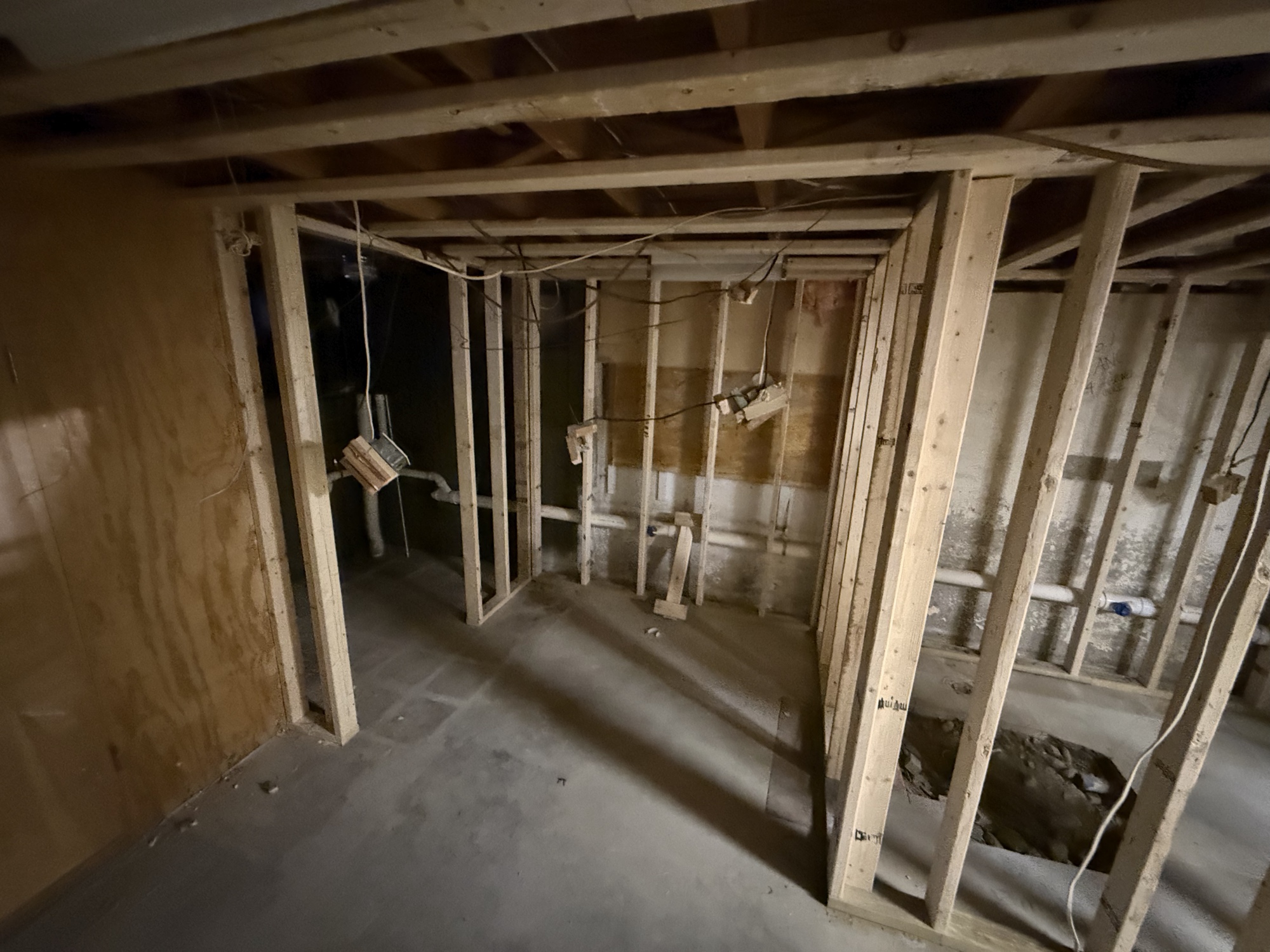 Unfinished basement framing with exposed studs and rough plumbing